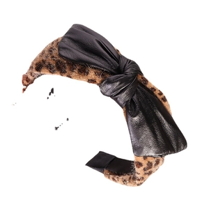 Leopard print headband with black faux leather bow accent on a minimalist background