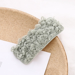 Close-up of light green plush faux fur rectangle hair clip on a textured fabric
