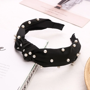 Détail d'un serre-tête noir noué orné de perles blanches sur un fond minimaliste