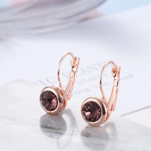 Gros plan de boucles d'oreilles or rose avec zircon violet rond sur une surface en marbre