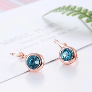 Détail de boucles d'oreilles rondes or rose avec cristal bleu foncé serti clos