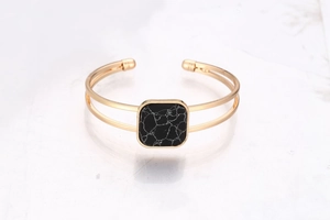 Detailed close-up of a double-layered gold cuff bracelet with a square black marble stone