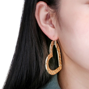 Gold hollow heart hoop earrings with vintage floral pattern worn by a model