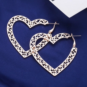 Rose gold heart hoop earrings with intricate floral cutouts on dark blue silk background