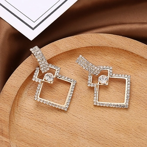 Détails de boucles d'oreilles géométriques en diamant sur plateau en bois et soie dorée