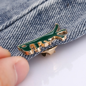 Cute green enamel dinosaur brooch pin on denim jacket with gold plated metal edges