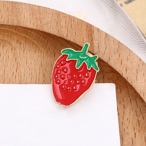 Vibrant red strawberry enamel brooch with gold-tone metal finish on wooden tray