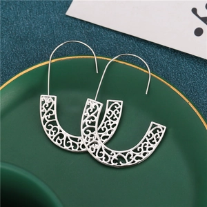 Silver geometric hollow hoop earrings with carved floral pattern on a green ceramic plate