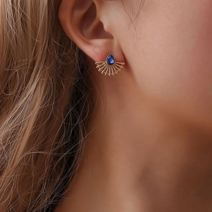 Close-up of gold fan-shaped stud earrings with blue teardrop gemstones on a female model