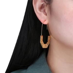 Golden geometric U-shaped hollow earrings with intricate patterns on a fashion model