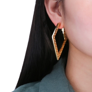 Close-up of a large gold geometric rhombus earring with intricate textured patterns