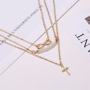 Détail d'un collier doré à trois rangs avec symbole infini, perles et pendentif croix