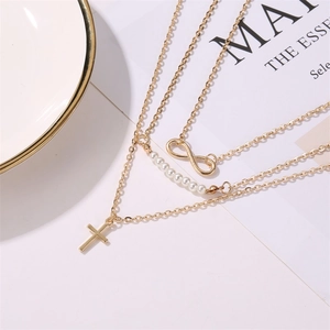 Détail d'un collier doré à trois rangs avec perles, symbole infini et pendentif croix