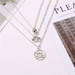 Macro shot of silver triple-layered necklace with intricate lotus pendants on white magazine