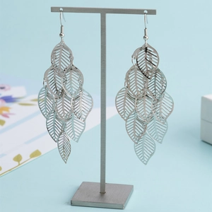 Boucles d'oreilles pendantes feuilles creuses argentées sur support avec fond bleu