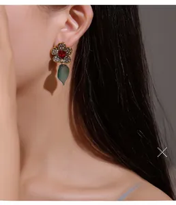 Detail eines Vintage Blumenohrrings mit Rubinstein und dunkelgrünem Blatt am Model