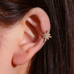 Sparkling gold star ear cuff with zircon inlays on a model's ear in close-up view