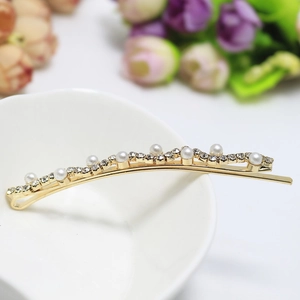 Détail d'une barrette dorée avec perles et strass posée sur un bol en céramique blanc