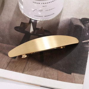 Barrette à cheveux ovale en métal doré brossé élégante posée sur un magazine chic