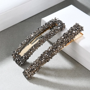 Close-up of vintage gold hair clip set featuring dark grey crystals on textured background