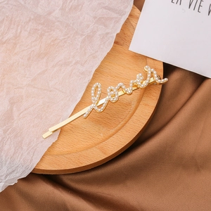 Détail d'une barrette Love dorée ornée de perles sur un fond en soie élégant et chic