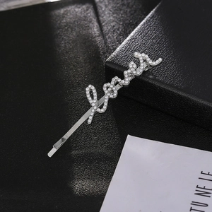 Détail macro d'une pince à cheveux argentée avec lettrage LOVE et perles blanches