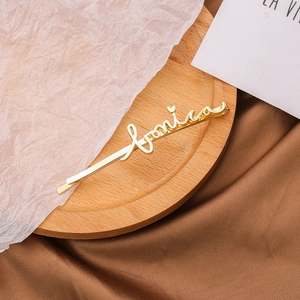 Détail d'une barrette dorée avec le prénom Monica en écriture cursive sur plateau en bois