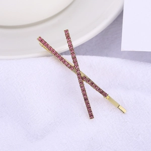 Close-up of golden X-shaped hair clips with micro-pave pink rhinestones on white fabric