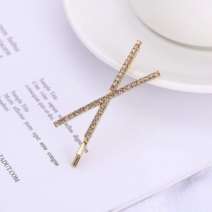 Elegant gold-tone cross X hair clip with champagne crystals on a magazine and cup