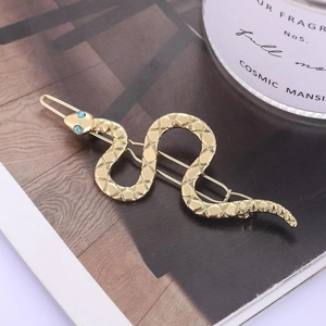 Golden snake-shaped hair clip with diamond patterns and blue gemstone eyes on magazine