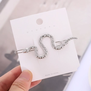 Silver snake-shaped metal hair clip with textured scales and crystal eyes on card