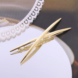 Pair of sleek metallic gold crisscross hair clips with mirror finish on a reflective base