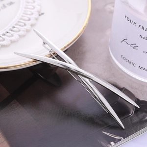 Minimalist silver X-shaped crossover hair clip with a polished metallic finish on a magazine