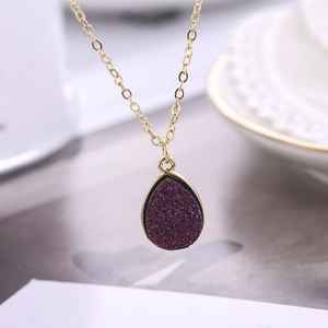 Vue macro d'un pendentif goutte doré avec pierre druzy violette sur une fine chaîne O