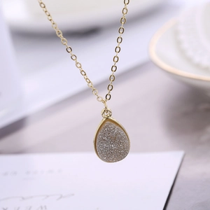 Gros plan d'un collier goutte doré avec un centre en cristal de style druzy scintillant