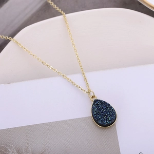 Détail d'un collier doré en forme de goutte d'eau avec pierre druzy bleue étincelante