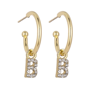 Close-up of golden C-shaped hoop earrings with sparkling pave-set letter B pendants