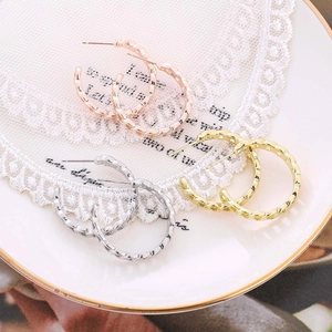 Detailed view of three pairs of twisted hoop earrings in rose gold, gold, and silver finishes