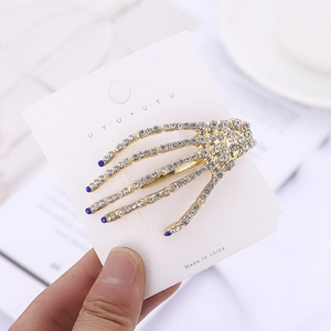 Detail showing golden skull hand hair clip with white and blue rhinestones on display card