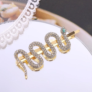 Golden snake hair clip with white crystals and green eye rhinestone on mirror surface