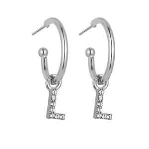 Macro detail of silver hoop earrings featuring sparkling diamond-encrusted letter L pendants