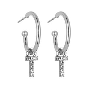 Detail showing polished silver-tone earrings with diamond-encrusted letter T pendants