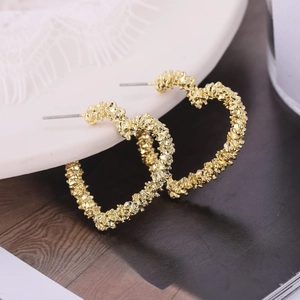 Détail de boucles d'oreilles cœur dorées texture lave sur plat céramique gaufré