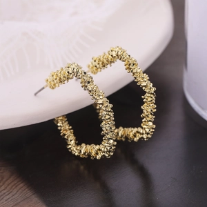 Détail de boucles d'oreilles dorées avec forme carrée irrégulière et texture lave