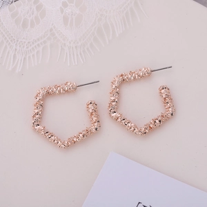 Détail de boucles d'oreilles C or rose avec une texture métallique plissée et polie unique