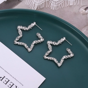 Gros plan de boucles d'oreilles étoile argentées texturées sur un plateau en céramique
