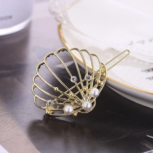 Détail de la pince à cheveux coquillage dorée avec perles et strass sur plat en céramique