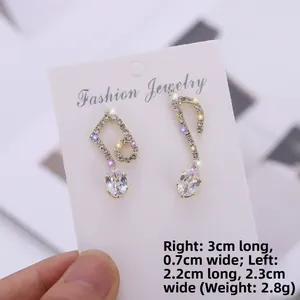 Detail of asymmetric music note earrings with zircons and 18K gold finish