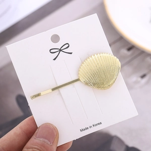 Barrette coquillage dorée minimaliste avec rayures verticales sur carte de support