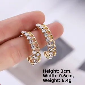 Détail de boucles d'oreilles créoles C dorées avec strass blancs, hauteur 3 cm